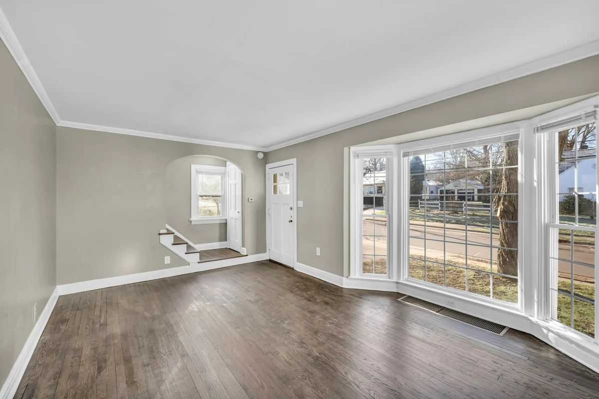 Empty living room with a dark wood floor, white trim and a bay window