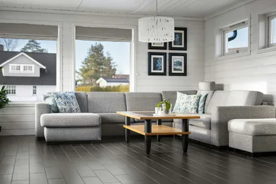 Living room with a dark gray plank floor, a gray sectional sofa and white shiplap walls