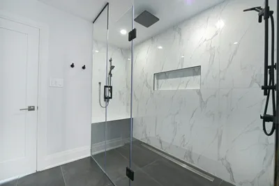 Walk in shower with large format marble look wall tile, a glass panel and a dark tiled floor